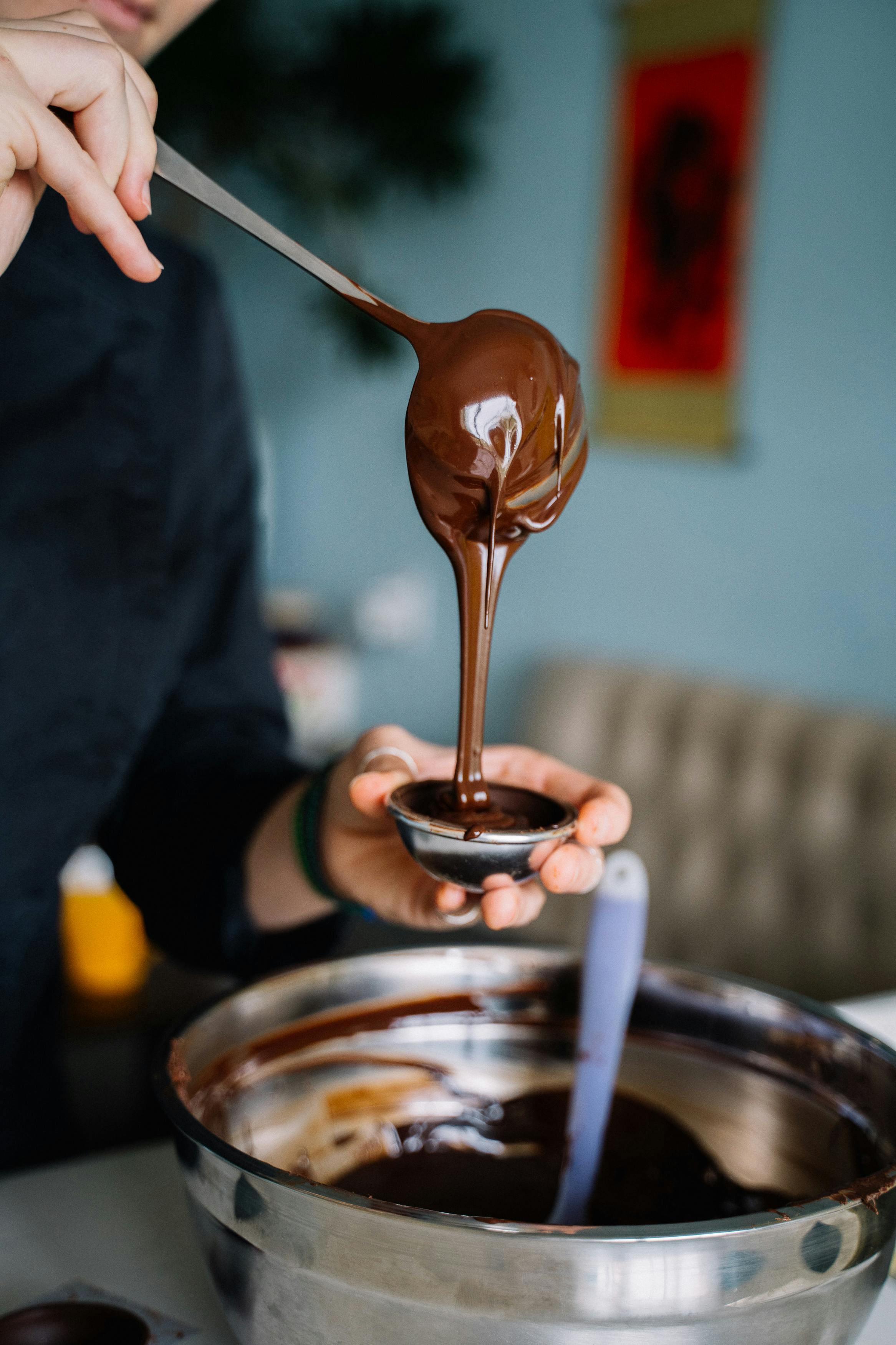 A person focused on tempering chocolate in a bowl in a bright, modern kitchen.